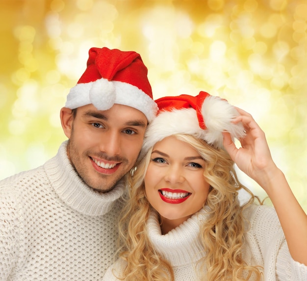 inverno, vacanze, natale e concetto di persone - coppia sorridente in maglioni e cappelli di Babbo Natale su sfondo di luci gialle