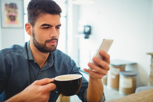 Invio di messaggi di testo del giovane sul telefono cellulare mentre mangiando caffè