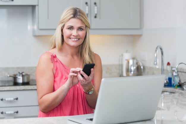 Invio di messaggi di testo della donna durante l&#39;utilizzo del computer portatile in cucina