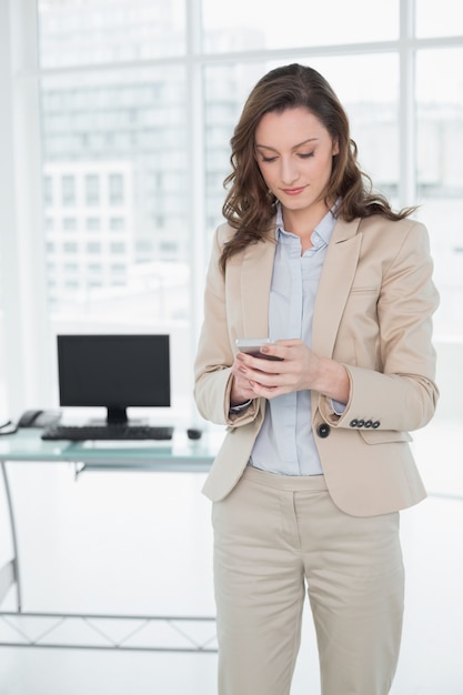 Invio di messaggi di testo elegante della donna di affari in un ufficio luminoso