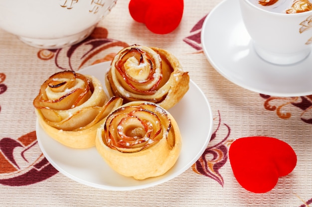 Involtini al forno rubicondo su un piatto bianco con una tazza di tè alla mela frutta