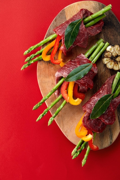 Involtini di manzo crudo e guarnizioni di verdure fresche pronte per la cottura su sfondo bianco