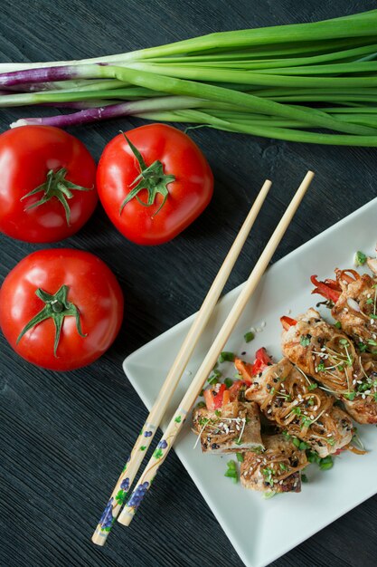 Involtini di petto di pollo al forno con erbe, fette di carote, peperone su un tagliere scuro. Stile asiatico. L'equilibrio di un'alimentazione sana. Cucinando. Sfondo di legno scuro