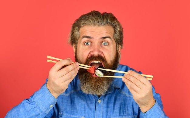 Involtini di sushi Cucina giapponese Pasto asiatico Rotolo di sushi L'uomo mangia le bacchette di sushi Cultura orientale Involtini di cibo hipster barbuto Consegna di cibo giapponese Zenzero in salamoia servito con sushi o sashimi