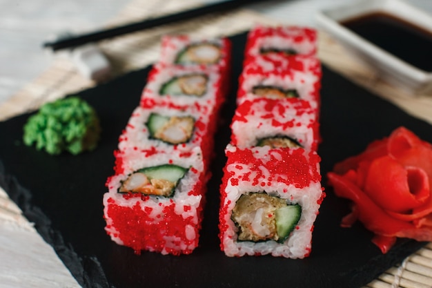 Involtini di sushi deliziosi appetitosi con tobiko rosso serviti su ardesia nera, primo piano. Cibo tradizionale e sano giapponese.