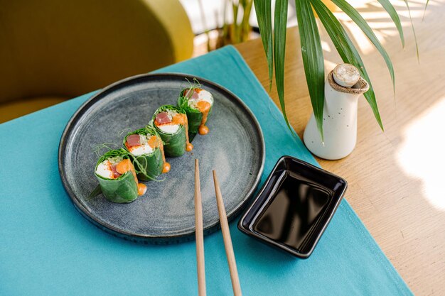 Involtini di sushi freschi e gustosi con salmone a foglie verdi e salsa succosa sul tavolo servito al ristorante di sushi con un bellissimo fulmine a contrasto