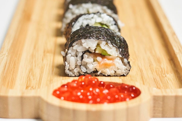Involtini di sushi maki freschi e appetitosi serviti con caviale rosso su un piatto di legno