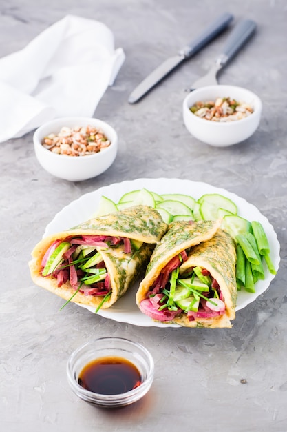 Involtini di uova ripieni di pastrami, verdure e cipolle verdi su un piatto, grani germogliati e salsa di soia in ciotole sul tavolo.