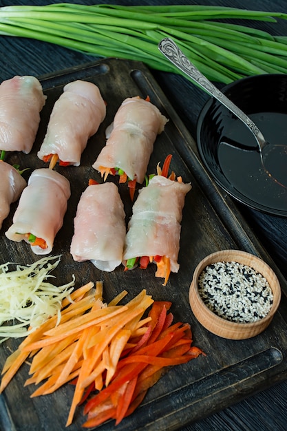 Involtini fatti in casa con petto di pollo fresco con verdure, fette di carota, peperone su un tagliere scuro.