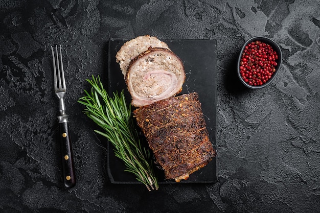 Involtino di maiale al forno Carne di maiale arrotolata con porchetta su tavola di marmo con erbe aromatiche Sfondo nero Vista dall'alto