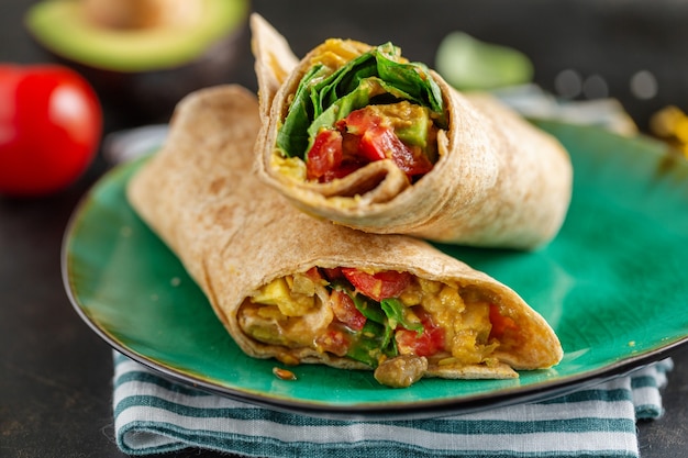 Involtino vegetariano vegano fresco gustoso con spinaci, pomodoro, avocado servito su piatto.