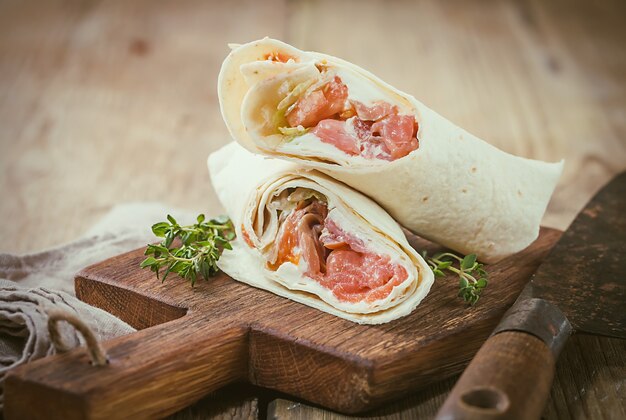 Involucro di tortilla fresca con verdure e salmone sul tagliere di legno