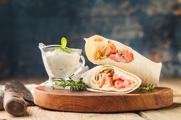 Involucro di tortilla fresca con verdure e salmone sul tagliere di legno