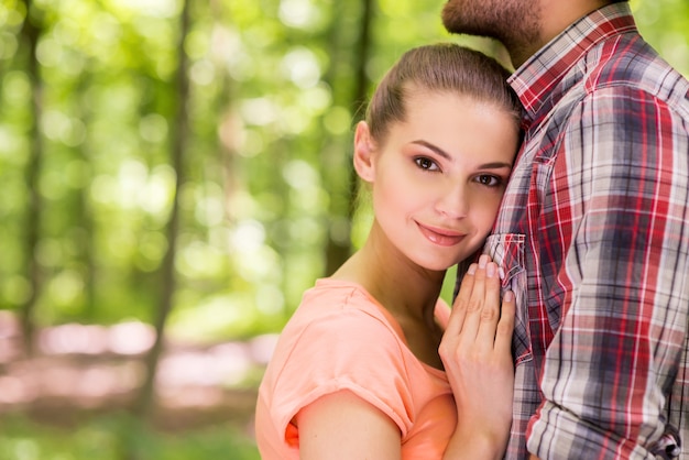 Io lo amo così tanto! Bella giovane donna che si appoggia al petto del suo ragazzo e sorride mentre sta insieme in un parco