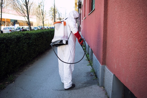 Irriconoscibile lavoratore in tuta di protezione chimica che spruzza disinfettante su superfici pubbliche.