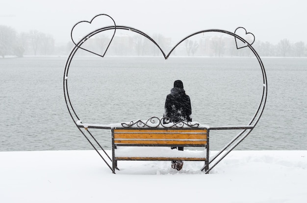 Irriconoscibile ragazza seduta sulla bellissima panchina in ferro battuto dell'amore nel parco con laghetto e godendo di una bellissima giornata invernale in solitudine