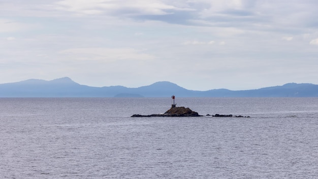 Isola rocciosa con l'oceano del faro e le montagne in una giornata nuvolosa