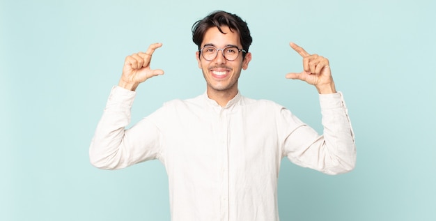 Ispanico bell'uomo che incornicia o delinea il proprio sorriso con entrambe le mani, guardando positivo e felice, concetto di benessere