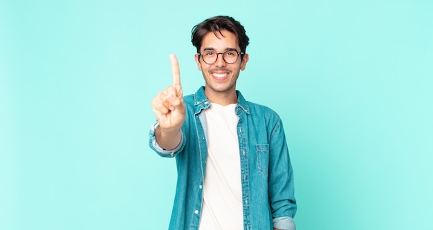 Ispanico bell'uomo sorridente e dall'aspetto amichevole, mostrando il numero uno o il primo con la mano in avanti, conto alla rovescia