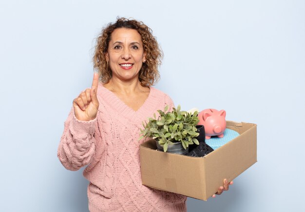 Ispanico donna di mezza età sorridente e guardando amichevole, mostrando il numero uno o il primo con la mano in avanti, conto alla rovescia