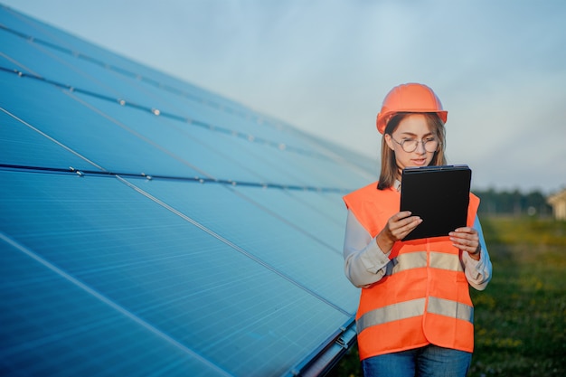 Ispettore ingegnere donna che tiene tavoletta digitale lavorando in pannelli solari Power Farm, parco di celle fotovoltaiche, concetto di energia verde.