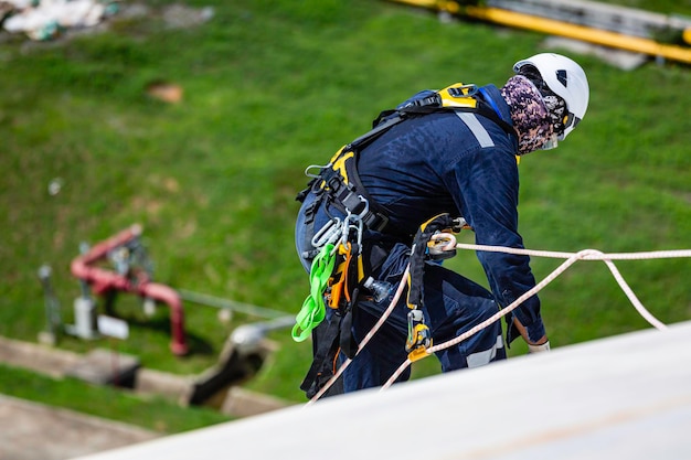 Ispezione del lavoratore di sesso maschile che indossa la prima linea di sicurezza della fune dell'imbracatura di sicurezza che lavora in un punto elevato sul gas sferico del tetto del serbatoio