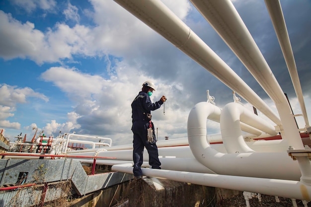 Ispezione del lavoratore di sesso maschile su tubi lunghi in acciaio e gomito del tubo nella fabbrica di petrolio della stazione durante la valvola di raffineria del controllo visivo registra l'olio e il gas dell'oleodotto