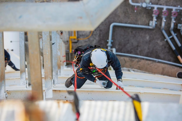 Ispezione del lavoratore maschio vista dall'alto che indossa la prima linea di sicurezza della fune dell'imbracatura di sicurezza che lavora in un punto alto sul tetto del serbatoio sferico