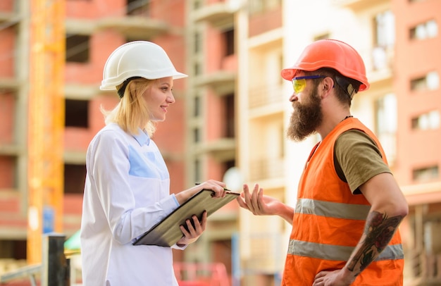 Ispezione del progetto di costruzione Concetto di ispettore di sicurezza Ispettore donna e costruttore brutale barbuto discutono dei progressi della costruzione Ispezione di sicurezza del cantiere Discutere il progetto di avanzamento