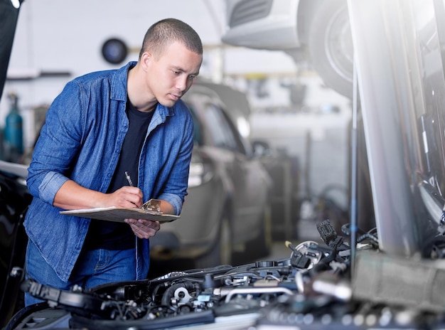 Ispezione del servizio auto e meccanico in auto con appunti che controllano il motore Ingegnere tecnico e uomo che lavora in garage o in officina scrivendo appunti per la manutenzione della riparazione e la cura del motore per il veicolo