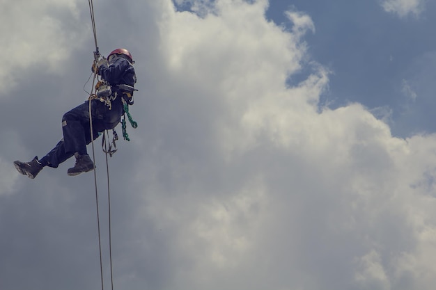 Ispezione dell'accesso alla fune del lavoratore maschio del cielo blu del fondo dell'industria del serbatoio di stoccaggio dello spessore