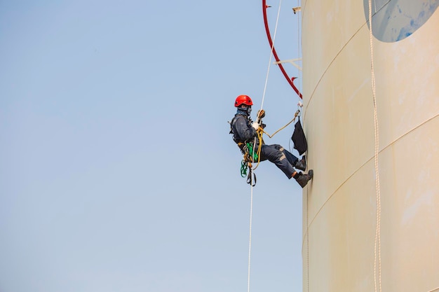 Ispezione dell'accesso alla fune del lavoratore maschio dell'industria del serbatoio di stoccaggio dello spessore