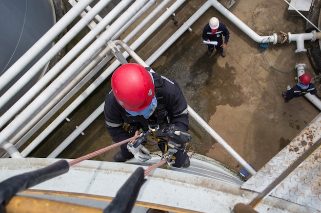 Ispezione di accesso alla fune del lavoratore maschio vista dall'alto dell'industria del serbatoio di stoccaggio dello spessore sotto l'olio della conduttura