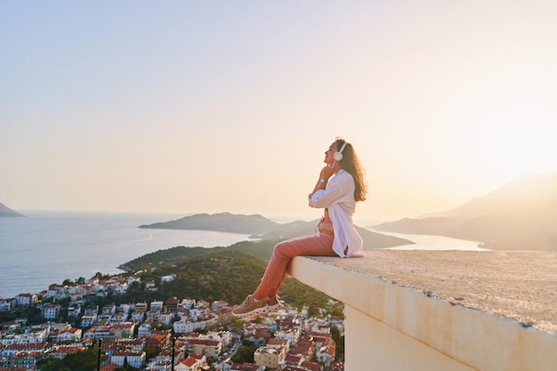 Ispirata donna felice seduta in cima e godendo di ascoltare musica calma con splendida vista al tramonto Sollievo dallo stress e menti sane