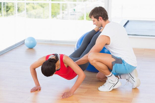 Istruttore che aiuta giovane donna con la palla di forma fisica alla palestra