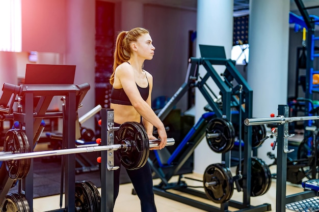 Istruttore di fitness giovane sexy che si esercita in palestra Ragazza di forma fisica che si esercita con il bilanciere in palestra