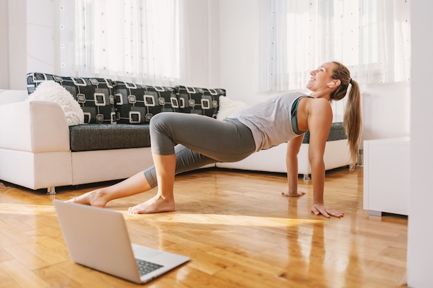 Istruttore di fitness muscolare sorridente seduto a casa sul pavimento e mostrando esercizi di stretching