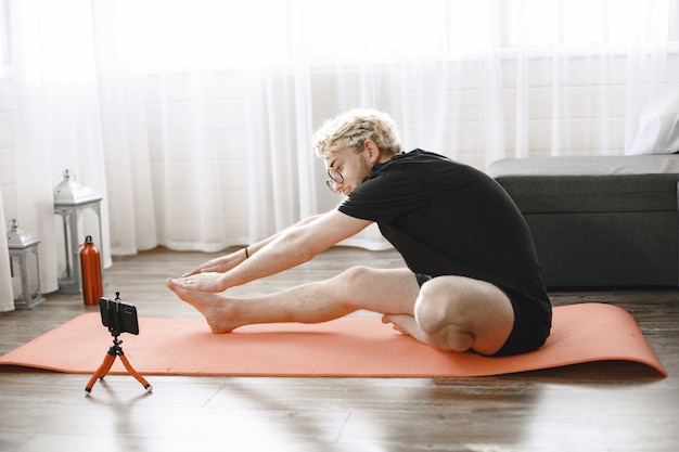 Istruttore di fitness o video blogger che fa stretching. L'uomo si sta riprendendo con la fotocamera dello smartphone a casa.