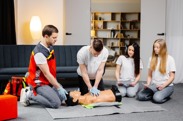 Istruttore di giovane uomo che aiuta a fare compressioni cardiache di primo soccorso con manichino durante l'allenamento di gruppo al chiuso