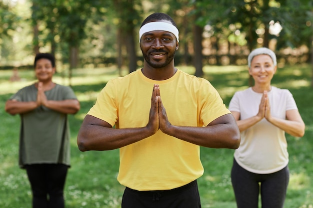 Istruttore di yoga maschio che sorride alla macchina fotografica nel parco con le donne anziane in background