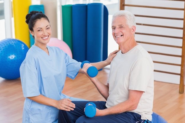 Istruttore femminile con l&#39;uomo senior che alza i dumbbells