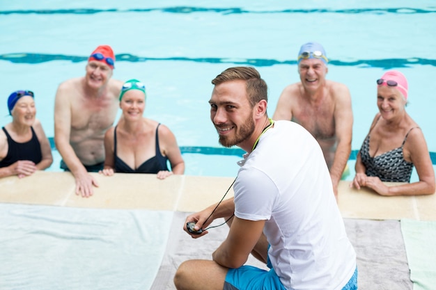 Istruttore maschio allegro che assiste i nuotatori senior a bordo piscina