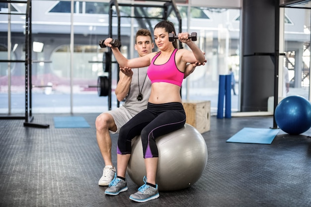 Istruttore maschio che assiste donna che alza i dumbbells alla palestra