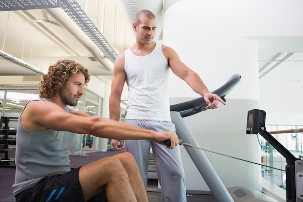 Istruttore maschio che assiste uomo sulla macchina di forma fisica alla palestra