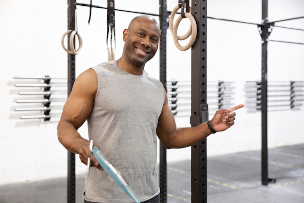 Istruttore maschio nero con atteggiamento positivo e sorridente. È nel centro fitness. Spazio per il testo.