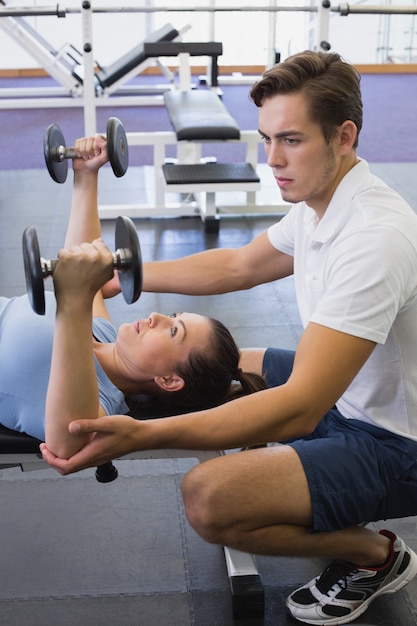 Istruttore personale che aiuta i dumbbells dell&#39;elevatore del cliente