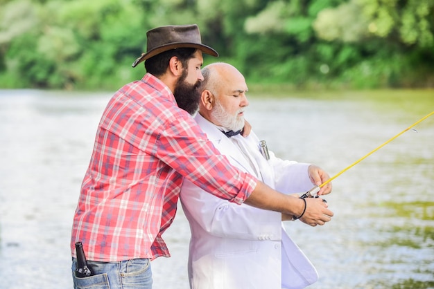 Istruttore personale Uomo barbuto ed elegante uomo d'affari pescano insieme Impara a pescare Pesca con un compagno che può offrire aiuto in caso di emergenza Abilità di pesca Uomini amici che si rilassano sullo sfondo della natura