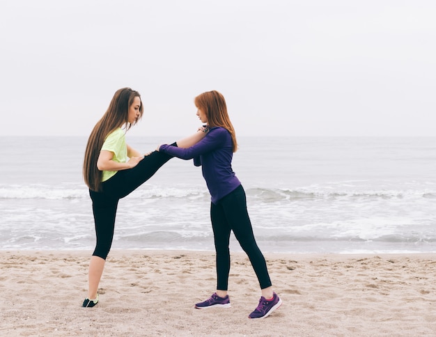 Istruttore sportivo aiuta la ragazza a fare stretching sulla spiaggia
