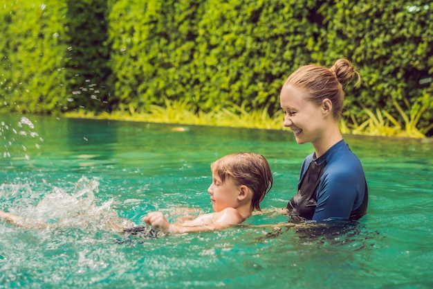 Istruttrice di nuoto per bambini sta insegnando a un ragazzo felice a nuotare in piscina