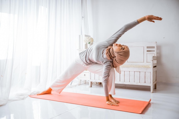 istruttrice musulmana asiatica che indossa l'hijab che fa yoga pilates posa tutorial su un materasso arancione in un